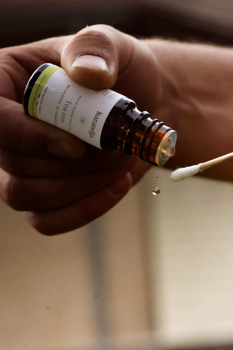 flacon d'huile essentielle Tea tree bio qui vide une goutte sur un coton tige