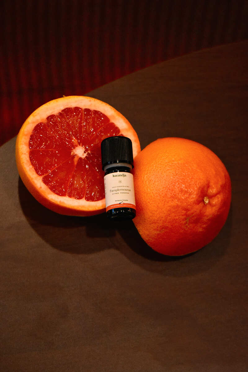 un flacon d'huile essentielle de pamplemousse posé sur un pamplemousse ouvert en deux