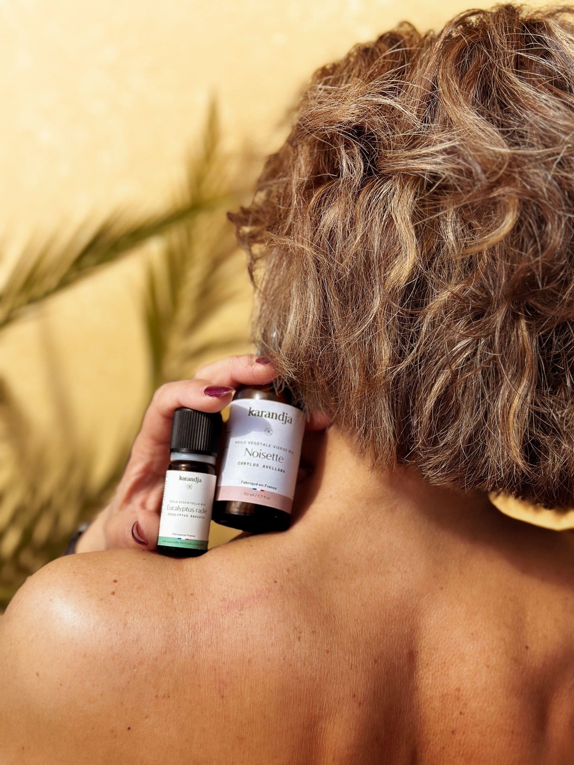 femme de dos tenant sur son épaule de l'huile essentielle eucalyptus radiata et huile végétale de noisette
