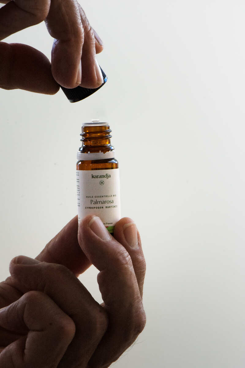 main qui tient un flacon huile essentielle palmarosa