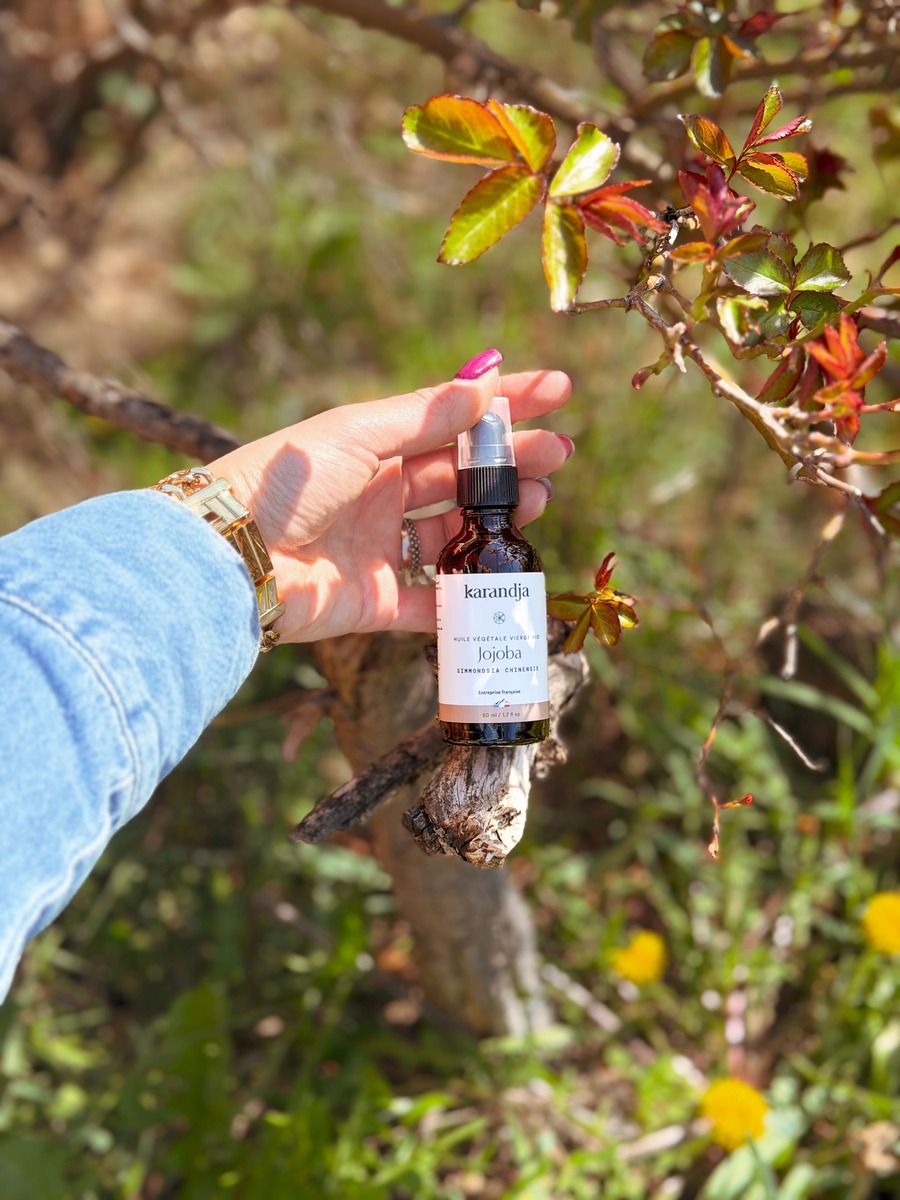 une main de femme qui tient un flacon d'huile végétale de jojoba bio